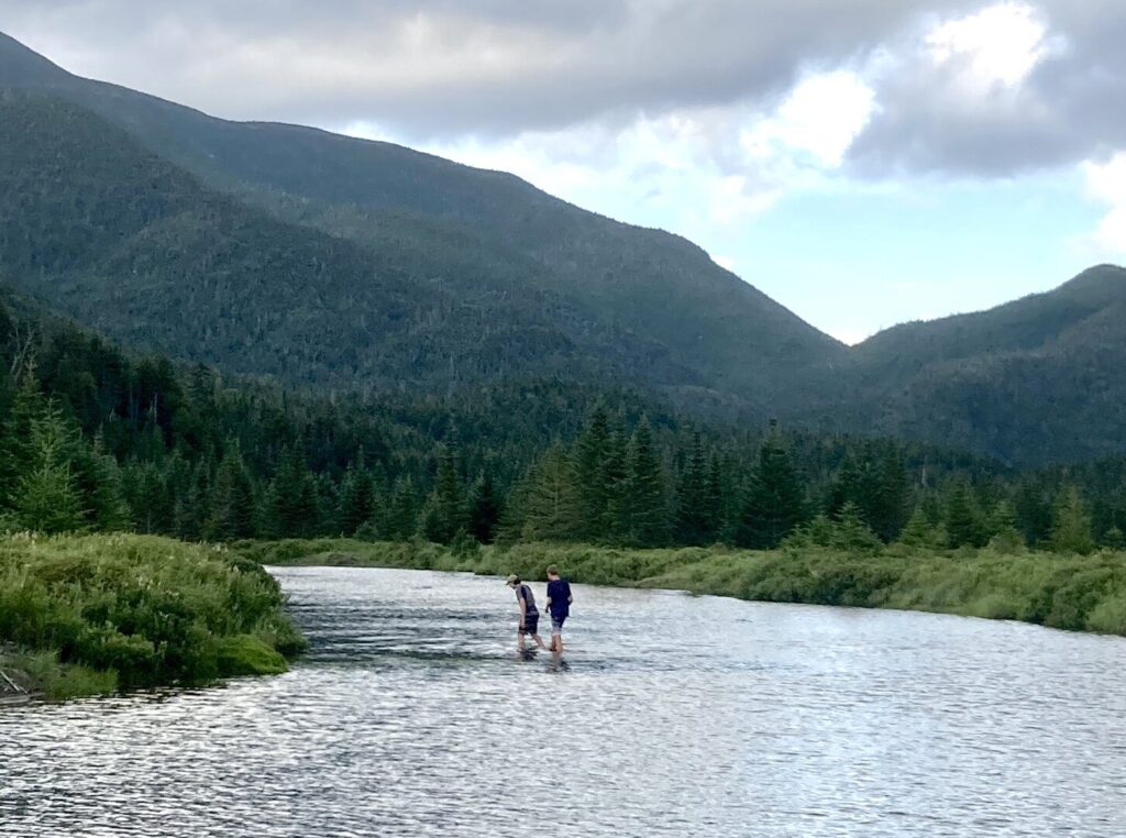 Two people standing ankle-deep in a lake with mountains in the backdrop